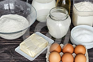Ingredients for pancakes: milk, eggs, sugar, salt, flour, vegetable oil on a wooden white background.