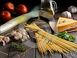 Ingredients for the preparation of pasta located on a dark wooden surface. Spaghetti, fresh vegetables, spices and olive oil for