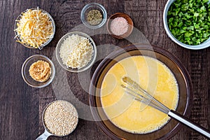 Ingredients for quinoa egg bake, raw egg mix in glass bowl with metal whisk, quinoa, cheese, herbs, broccoli, on a wood table photo