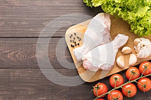 Ingredients and raw chicken leg on cutting board on wooden background