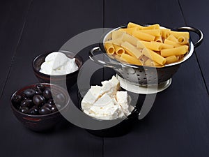 Ingredients for rigatoni with cream, gorgonzola and olives, set on a dark brown board photo