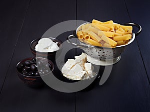 Ingredients for rigatoni with cream, gorgonzola and olives, set on a dark brown board photo