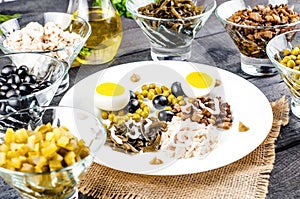 Ingredients for salad in transparent plates on a black wooden background. Fried champignons, olives, pickled cucumbers, chicken fi