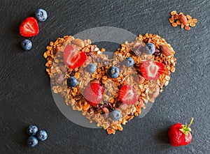 Ingredients in shape of heart to cook a breakfast. Blueberries, strawberries and granola made from oat flakes, dried fruits, nuts