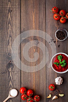 Ingredients for tomato sauce. Cherry tomatoes, garlic, green basil, black pepper, salt in spoon on dark wooden