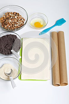 Ingredients and tools for making puff pastry curls stuffed with poppy and walnut. Are laid out on a white table top