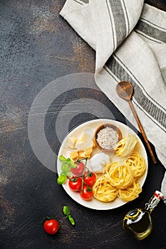 Ingredients for traditional Italian pasta dish. Uncooked raw tagliatelle bolognesi, parmesan cheese, olive oil, garlic, basil