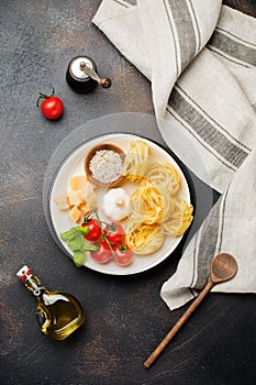 Ingredients for traditional Italian pasta dish. Uncooked raw tagliatelle bolognesi, parmesan cheese, olive oil, garlic, basil