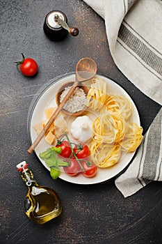 Ingredients for traditional Italian pasta dish. Uncooked raw tagliatelle bolognesi, parmesan cheese, olive oil, garlic, basil