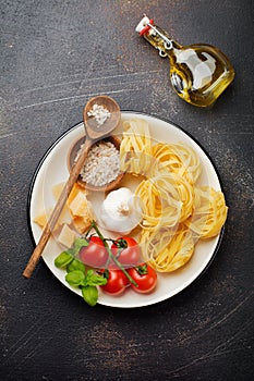 Ingredients for traditional Italian pasta dish. Uncooked raw tagliatelle bolognesi, parmesan cheese, olive oil, garlic, basil