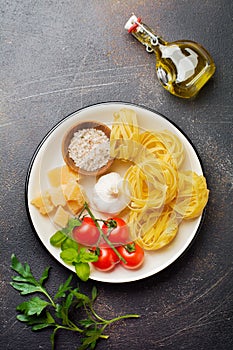 Ingredients for traditional Italian pasta dish. Uncooked raw tagliatelle bolognesi, parmesan cheese, olive oil, garlic, basil