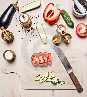 Ingredients for vegetarian salad, cucumbers, eggplant, red bell pepper, tomatoes, spices and herbs, lies next to cutting board a