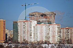 The inhabited skyscraper with the tower crane against the background of the old multi-storey building is under construction.