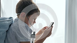 Inhalation medication, boy in mask from an inhaler with cell phone into hands