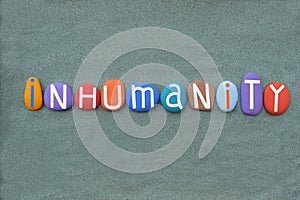 Inhumanity, creative text composed with multi colored stone letters over green sand