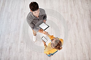 Initiating a new connection together. High angle shot of two young designers shaking hands while using digital devices