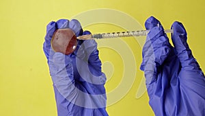 Injection into an grape. Hand in medical glove with syringe on yellow background. Genetic modified foods. Injection of GMOs