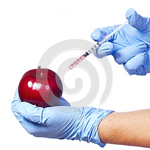 Injection into red apple isolated on white background. Genetically modified fruit and syringe