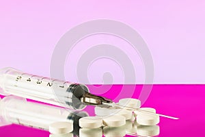 injection syringe with needle and white pills on pink background
