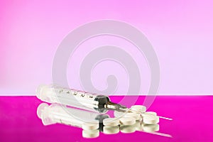 injection syringe with needle and white pills on pink background