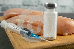 Injection syringe in raw chicken pieces, concept of injection of GMOs into the meat. Close-up