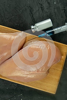 Injection syringe in raw chicken pieces, concept of injection of GMOs into the meat. Close-up