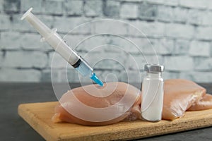 Injection syringe in raw chicken pieces, concept of injection of GMOs into the meat. Close-up