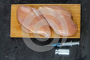 Injection syringe in raw chicken pieces, concept of injection of GMOs into the meat. Close-up