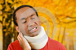 Injured black hispanic male wearing neck brace, holding hands in pain around support making faces of agony, yellow