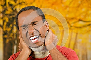 Injured black hispanic male wearing neck brace, holding hands in pain around support making faces of agony, yellow