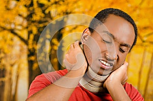 Injured black hispanic male wearing neck brace, holding hands in pain around support making faces of agony, yellow