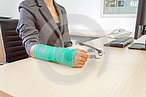 Injured businesswoman with green cast on the wrist holding white
