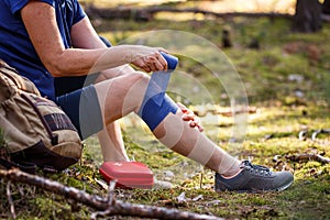 Injured hiker putting elastic bandage to her knee