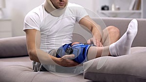 Injured man in foam cervical collar checking neoprene knee brace, rehabilitation