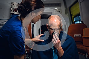An injured man pressing an oxygen mask to his face, a female paramedic is trying to calm him down