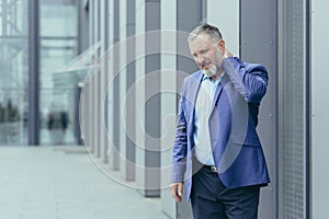 Injured and overtired senior gray-haired businessman, man outside office has severe neck pain photo