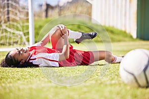 Injured, pain or injury of a female soccer player lying on a field holding her knee during a match. Hurt woman