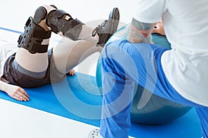 Injured patient in a leg brace exercising on a blue mat