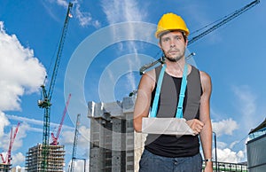 Injured worker is wearing medical sling on his arm. Construction site in background