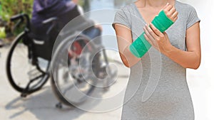Injury woman wearing sportsware with green cast on arm on blurred background female sitting on wheelchair, body injury concept.