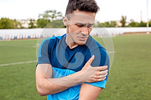 Injury. Young man on stadium outside standing touching hurted shoulder close-up