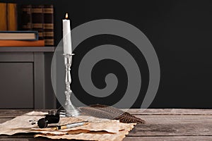 Inkwell, feather, fountain pen, candlestick and vintage parchment with ink stains on wooden table indoors. Space for text