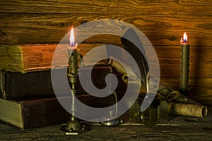 The inkwell with a feather, old documents and books, burning candles stand on a wooden table