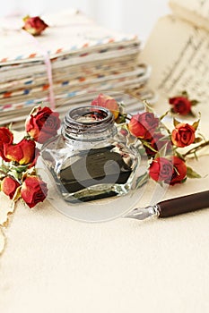 Inkwell, pen, dried roses and stack of vintage letters