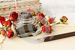 Inkwell, pen and dried roses on vintage paper background. Love letters idea