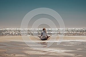 Inner balance life concept with woman sitting at the beach doing yoga meditation relax position viewed from back. Blue sky and