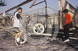 Inner city youth riding bicycle at burned out building, South Central Los Angeles, California