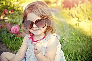 Innocence, purity and youth. Girl in sunglasses sitting in park on floral environment