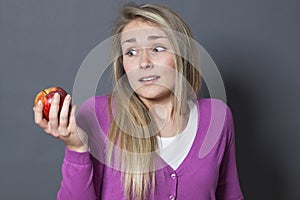 Innocent blonde girl resisting in eating an appetizing apple
