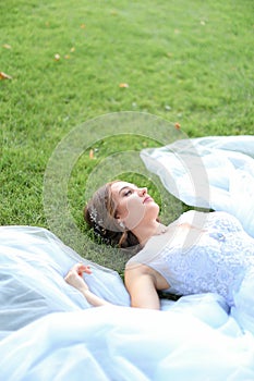 Innocent bride lying on grass in oark and wearing white dress.